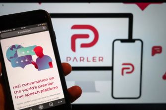 Image showing a smartphone displaying the Parler website alongside a large screen showcasing the Parler logo, emphasizing its branding as a free speech platform.