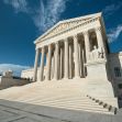 The United States Supreme Court building with its prominent columns and steps under a blue sky. The United States Supreme Court building with its prominent columns and steps under a blue sky.