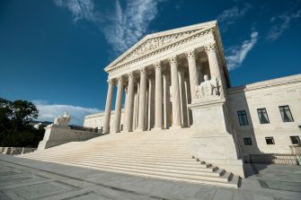 The United States Supreme Court building with its prominent columns and steps under a blue sky.