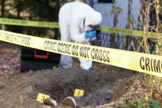 A forensic investigator collecting evidence at a crime scene marked with "DO NOT CROSS" tape.