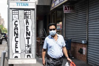 A man wearing a mask walks past a street mural calling for the cancellation of rent during the COVID-19 pandemic.