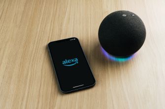 An Amazon Alexa device next to a smartphone displaying the Alexa app on a wooden surface.