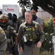 A group of law enforcement officers, including masked agents, conducting an operation in a public area in Southern California. A group of law enforcement officers, including masked agents, conducting an operation in a public area in Southern California.
