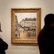 A painting by Camille Pissarro displayed at an art museum, with two visitors observing it. A painting by Camille Pissarro displayed at an art museum, with two visitors observing it.