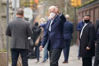 President Biden giving a thumbs up while walking outside, surrounded by people wearing masks.