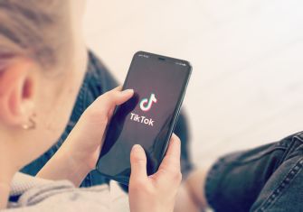 A person holding a smartphone displaying the TikTok logo on the screen.