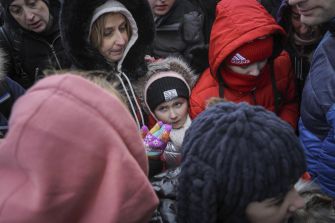 A group of Ukrainian asylum seekers, including children and adults, huddled together for warmth amid winter conditions while waiting for assistance.