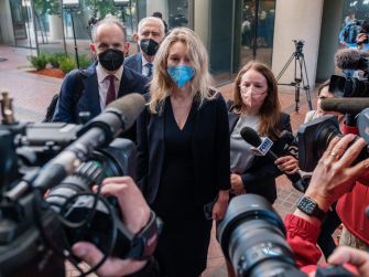 Elizabeth Holmes exiting the courthouse surrounded by media and legal representatives during her trial proceedings.
