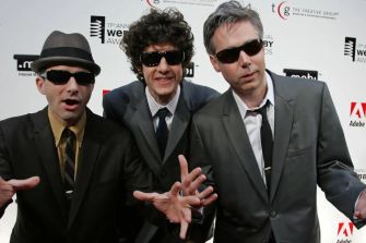 Three men in suits with sunglasses and hats pose together at an event.