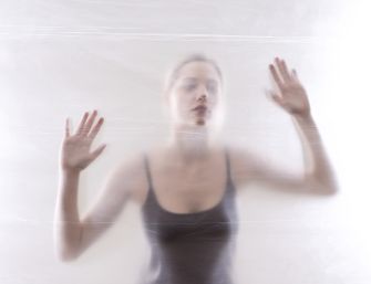 A blurred image of a young woman pressing her hands against a translucent surface, conveying a sense of isolation or entrapment.