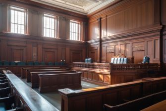 A view of an empty courtroom, showcasing wooden benches and the judge's bench illuminated by natural light.
