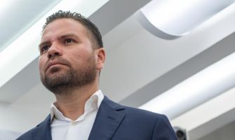 A man in a business suit looks solemnly ahead, possibly during a legal proceeding or press conference.