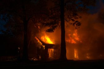 A house engulfed in flames during a fire incident at night, surrounded by trees.