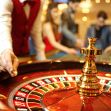 A close-up view of a roulette table in a casino, with a dealer's hand poised to spin the wheel. A close-up view of a roulette table in a casino, with a dealer's hand poised to spin the wheel.