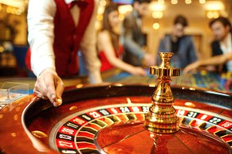 A close-up view of a roulette table in a casino, with a dealer's hand poised to spin the wheel.