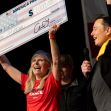 A woman holds a large check for one million dollars alongside Elon Musk at a promotional event for America PAC. A woman holds a large check for one million dollars alongside Elon Musk at a promotional event for America PAC.