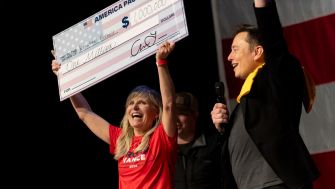 A woman holds a large check for one million dollars alongside Elon Musk at a promotional event for America PAC.
