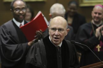 Former Georgia Chief Justice George H. Carley speaking at a public event, with attendees in the background.