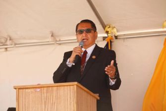 A person speaking at an event, holding a microphone, with a podium in front of them.