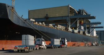 A cargo ship at dock with trucks unloading aluminum shipments.