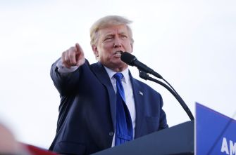 A man in a suit points while speaking at a microphone during an event.