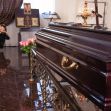 A closed casket in a funeral home setting, surrounded by flowers and memorial items. A closed casket in a funeral home setting, surrounded by flowers and memorial items.
