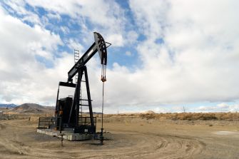An oil drilling pumpjack standing in a barren landscape under a cloudy sky.