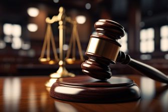 A wooden gavel on a desk in front of a scale of justice, symbolizing a courtroom setting.
