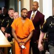 A man in handcuffs wearing an orange jumpsuit is being escorted through a courtroom by law enforcement officials. A man in handcuffs wearing an orange jumpsuit is being escorted through a courtroom by law enforcement officials.