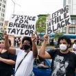 Two protesters holding signs that read "Justice for Breonna Taylor" and "Sleeping While Black" during a demonstration. Two protesters holding signs that read "Justice for Breonna Taylor" and "Sleeping While Black" during a demonstration.