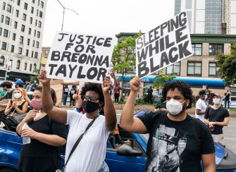 Two protesters holding signs that read "Justice for Breonna Taylor" and "Sleeping While Black" during a demonstration.