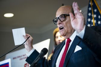 Rudy Giuliani speaking at a press conference, raising his hands while addressing the media.