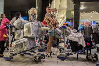 A family with children gathers at an airport terminal, surrounded by luggage on trolleys.