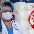 A healthcare worker wearing a mask and face shield stands in front of a COVID-19 safety tunnel. A healthcare worker wearing a mask and face shield stands in front of a COVID-19 safety tunnel.