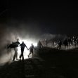 A group of individuals moving along a dusty path at night, illuminated by bright lights in the background. A group of individuals moving along a dusty path at night, illuminated by bright lights in the background.