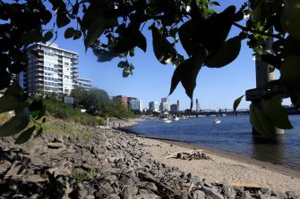 View of a sandy riverbank with rocks and urban buildings in the background, illustrating the Oregon waterway impacted by toxic PCB pollution.