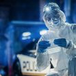 A forensic investigator in protective gear examines evidence at a crime scene, with a police vehicle in the background. A forensic investigator in protective gear examines evidence at a crime scene, with a police vehicle in the background.