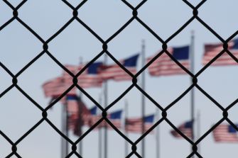 A blurred view of multiple American flags seen through a chain-link fence.