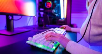 A person using a backlit keyboard and computer in a colorful gaming setup.