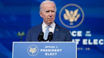 Joe Biden speaking at a podium labeled "Office of President Elect" with a serious expression.