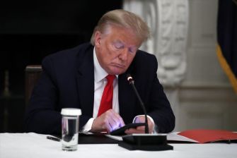 Donald Trump sitting at a table, looking down at his phone with a serious expression.