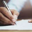 A hand holding a pen is seen writing on a sheet of paper, symbolizing the signing of a contract. A hand holding a pen is seen writing on a sheet of paper, symbolizing the signing of a contract.