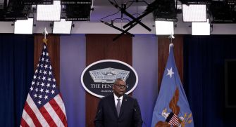 Defense Secretary Lloyd J. Austin III speaks at a podium with the Pentagon logo, flanked by the American flag and an Air Force flag.