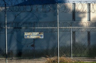 A view of the exterior of Alameda County Jail, featuring a "No Trespassing" sign and barbed wire fencing.