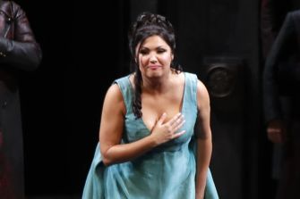Anna Netrebko performing on stage, wearing a blue dress and bowing to the audience.