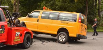 Image of a yellow school van on a tow truck, with police presence at the scene.
