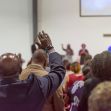 A congregation engaged in worship, with individuals raising their hands in a church setting. A congregation engaged in worship, with individuals raising their hands in a church setting.