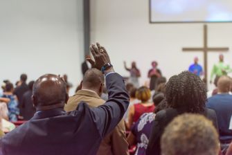 A congregation engaged in worship, with individuals raising their hands in a church setting.