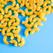A close-up of uncooked yellow macaroni noodles on a blue background. A close-up of uncooked yellow macaroni noodles on a blue background.