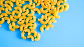A close-up of uncooked yellow macaroni noodles on a blue background.